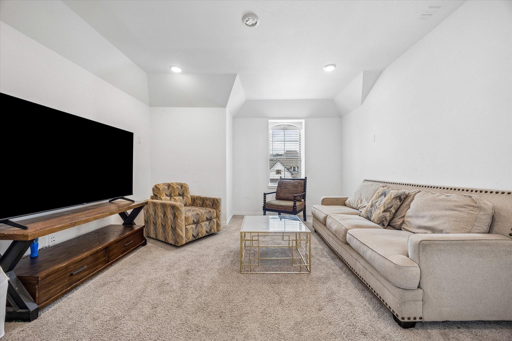 Living room with a large television, beige sofa, patterned armchairs, and high angled ceiling.
