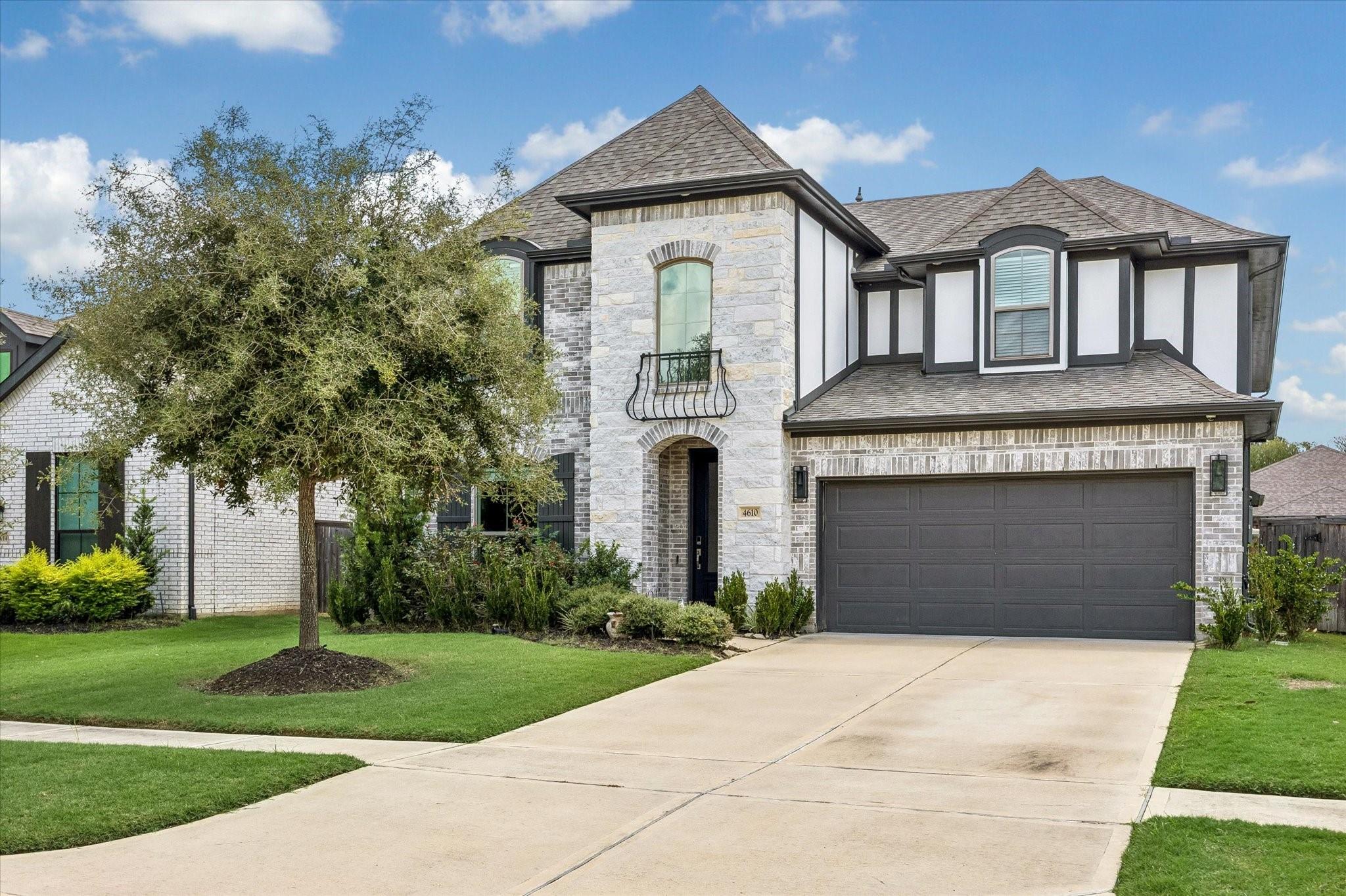 Two-story stone-and-white house with dark trim, a two-car garage, and a tree-shaded front lawn.