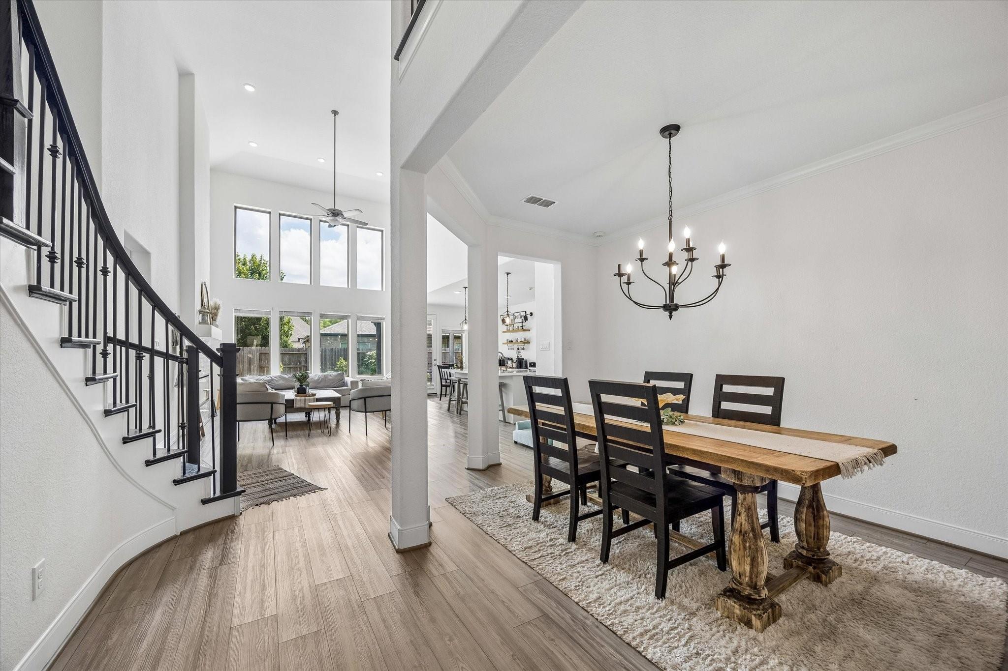 Open-plan dining area with a rustic wood table, black chandelier, and staircase beside a bright living room.