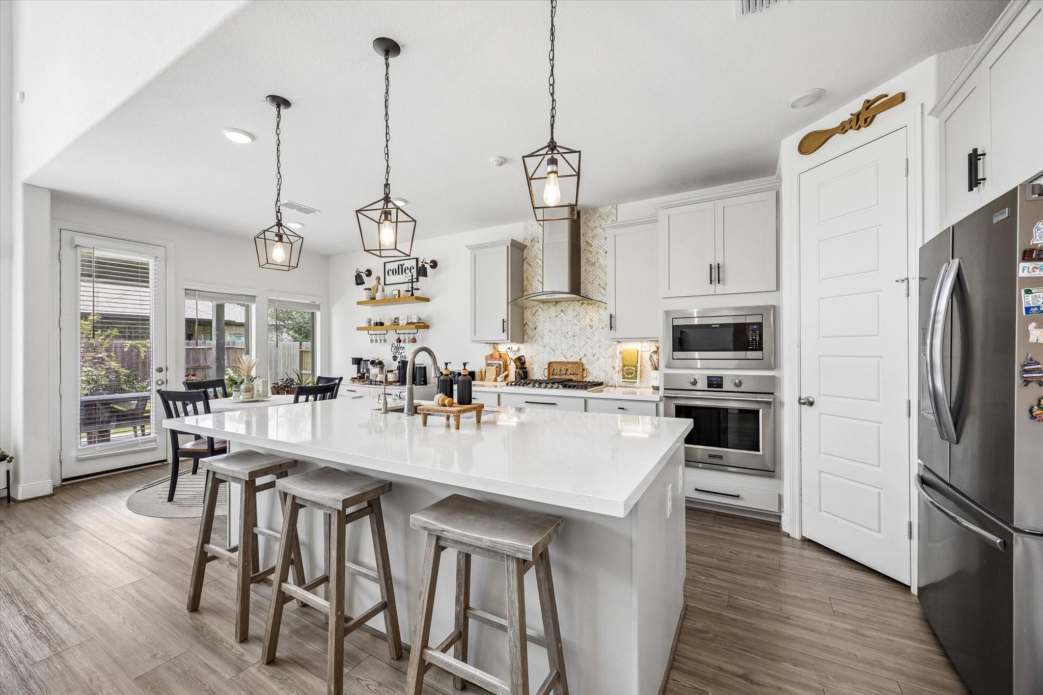 Bright white kitchen with a large island, bar stools, stainless appliances, and herringbone backsplash.