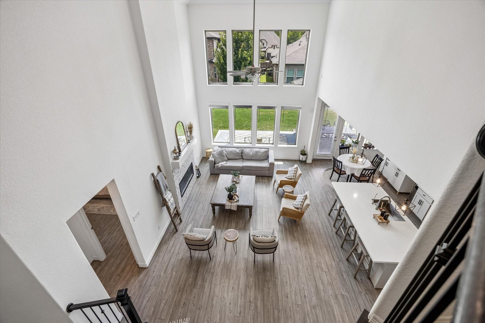 Double-height living room with fireplace, tall windows, and open kitchen and dining area.