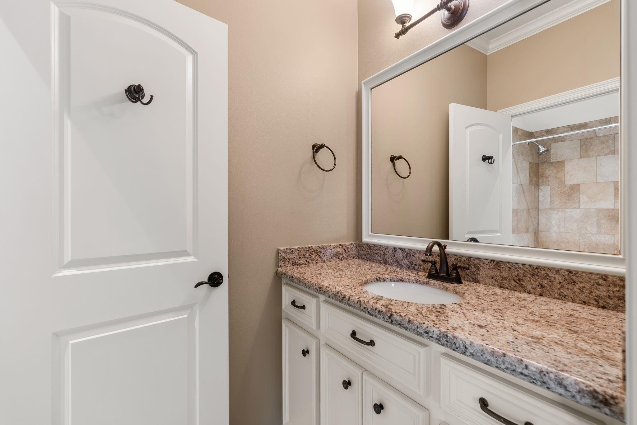 Bathroom vanity with speckled granite countertop and mirror reflecting a tiled shower.