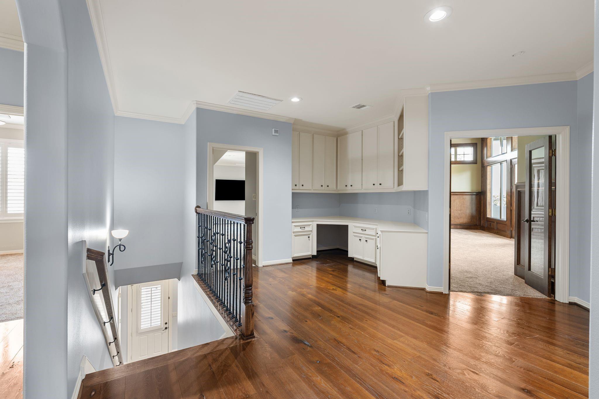 Upstairs landing with white built-in cabinetry, hardwood floors, and an ornate iron stair railing.