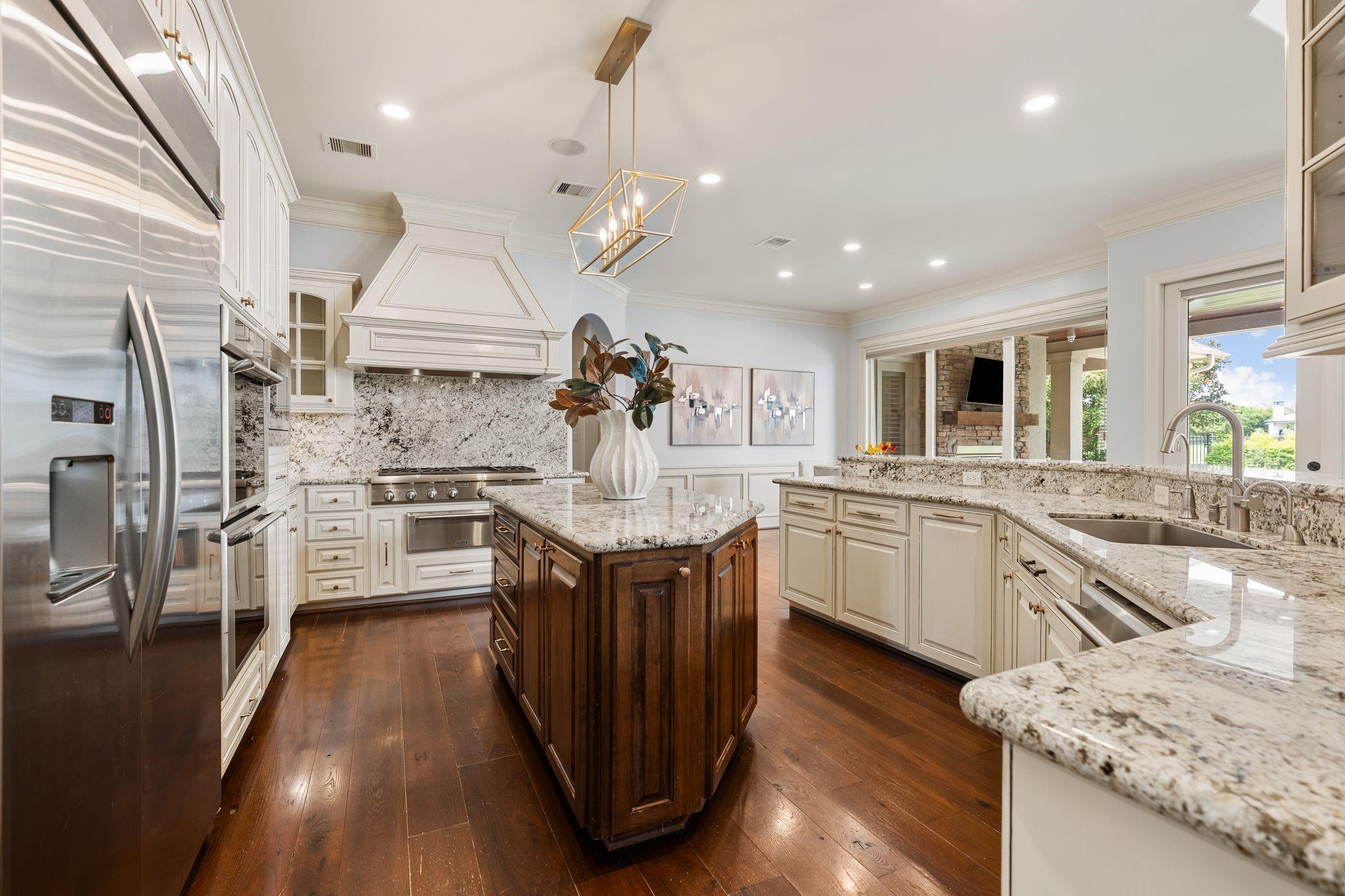 Bright kitchen with a dark wood island, white cabinetry, granite counters, and stainless steel appliances.