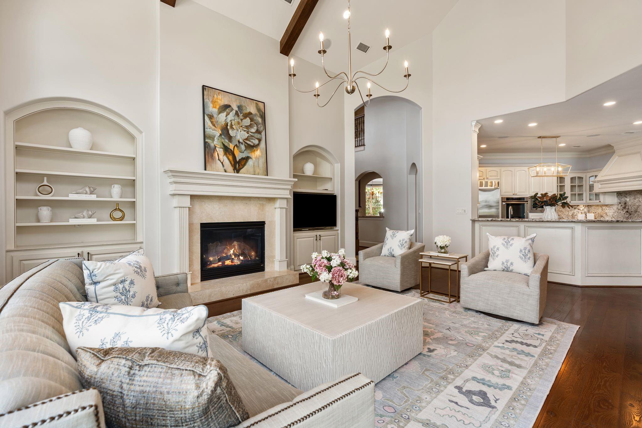 Living room with a vaulted ceiling, fireplace, built-in shelves, and open kitchen.