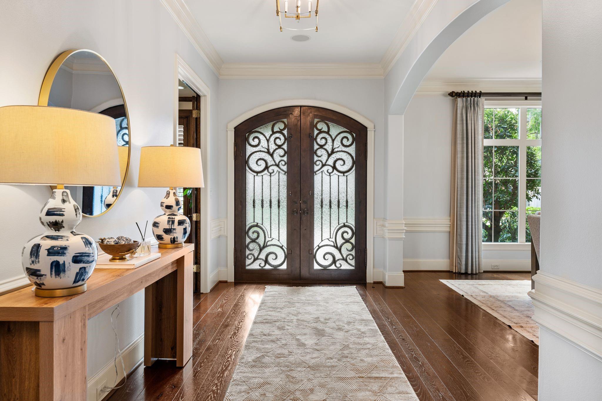 Foyer with ornate arched double doors, a console table, and a patterned runner on dark wood floors.