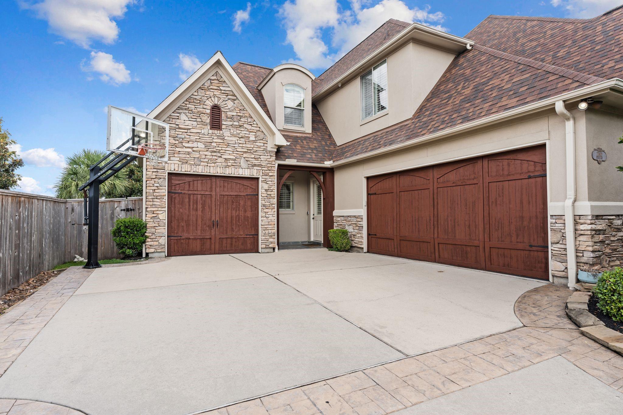 Two-story home with stone accents, wooden garage doors, and a basketball hoop beside the driveway.