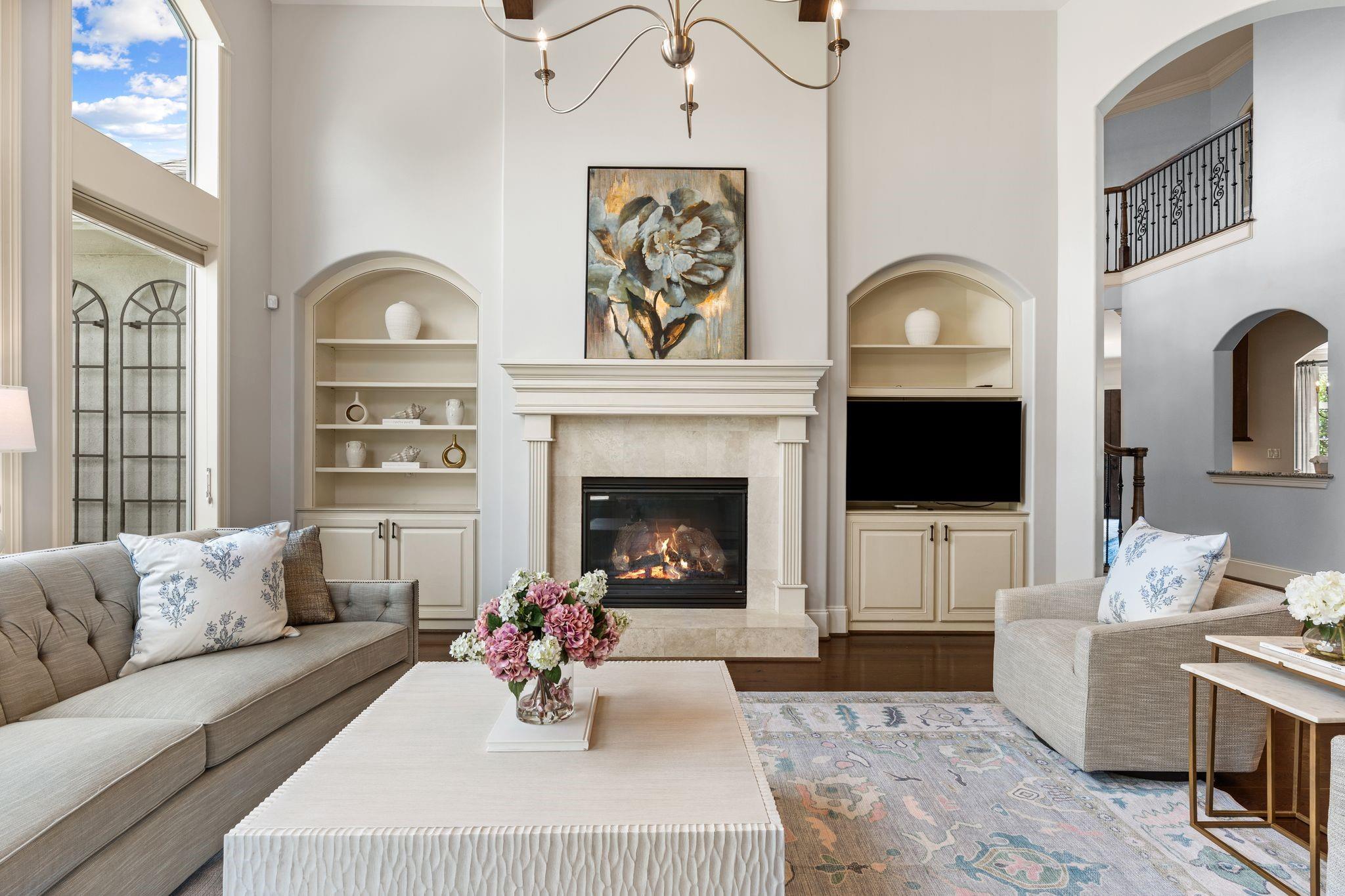 Staged living room with a central fireplace, vaulted ceiling, and cream built-in shelves.