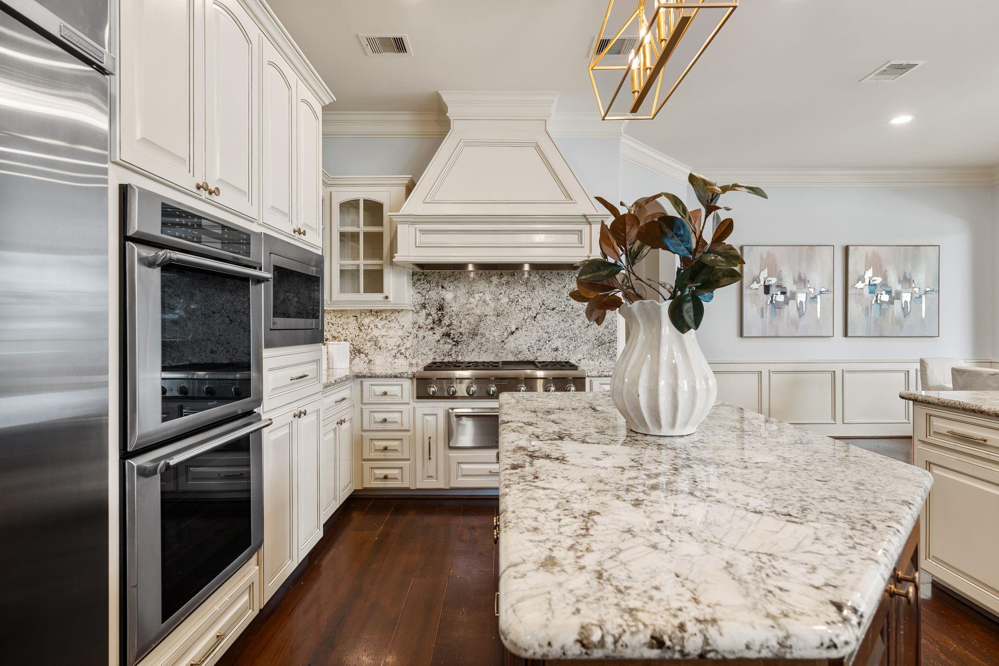 Kitchen with a large granite island, white cabinets, and stainless steel appliances.