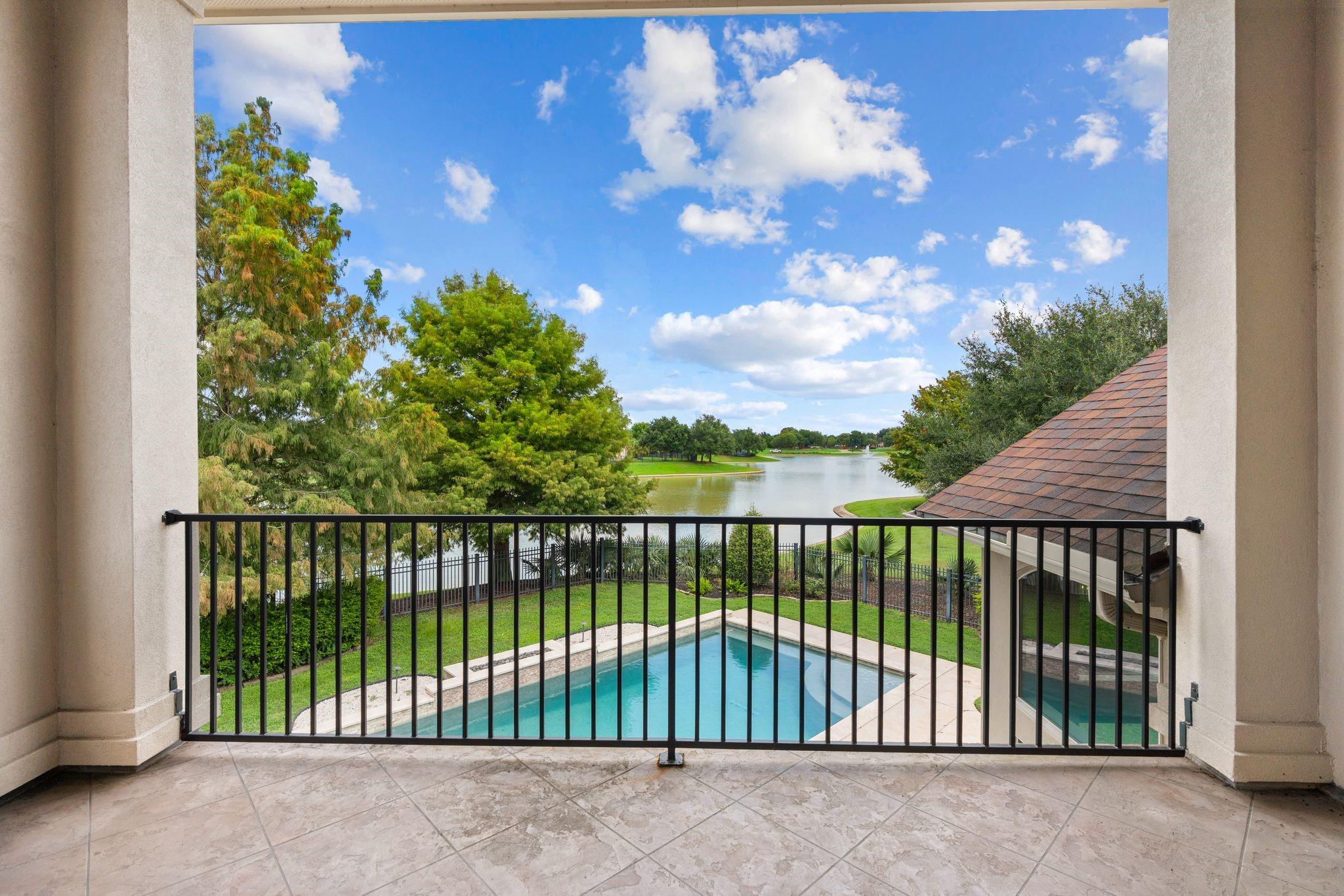 Balcony overlooking a backyard pool and lake, framed by leafy trees.