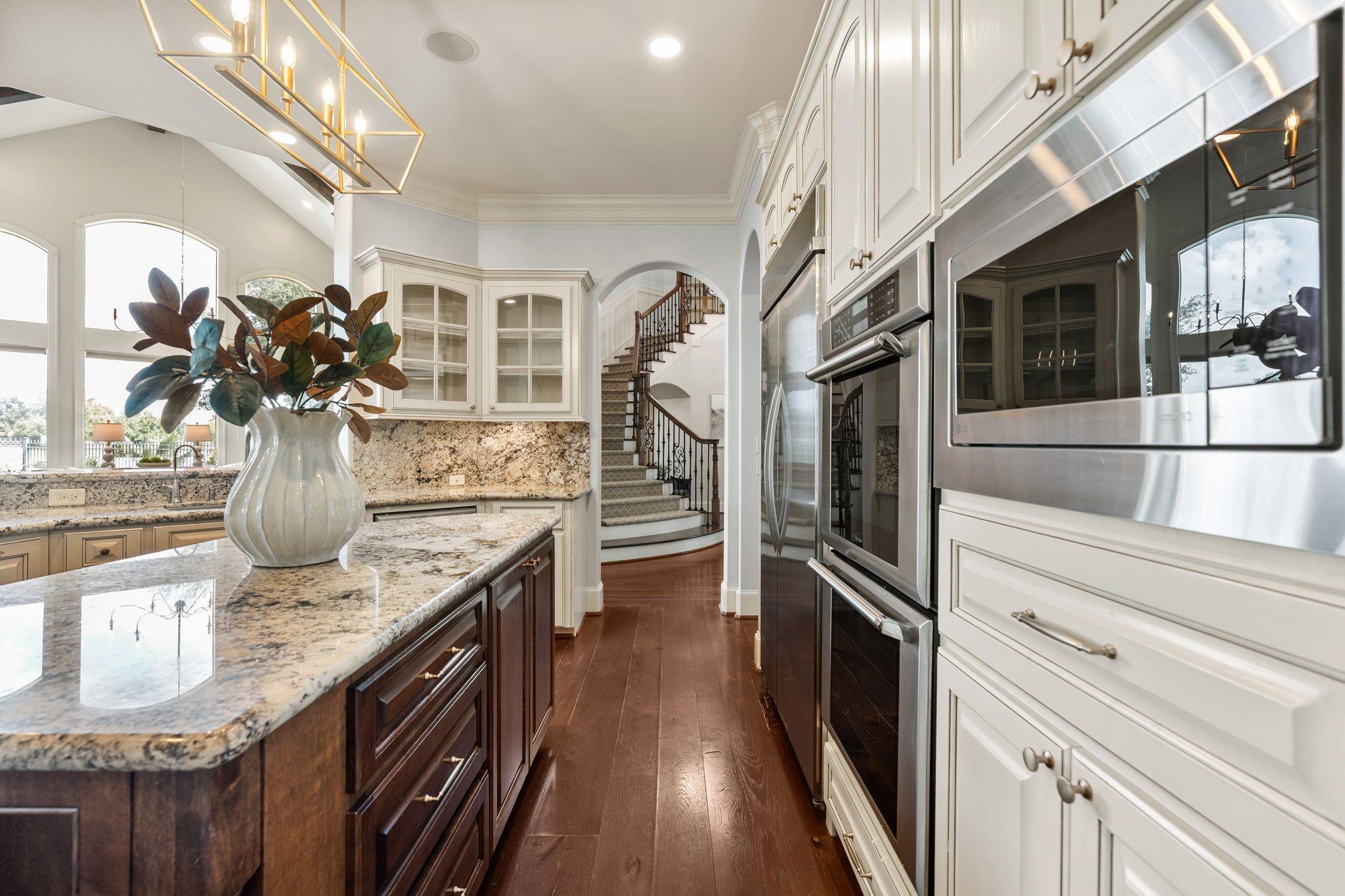 Kitchen with granite counters, stainless steel appliances, and a dark wood island beside tall windows.