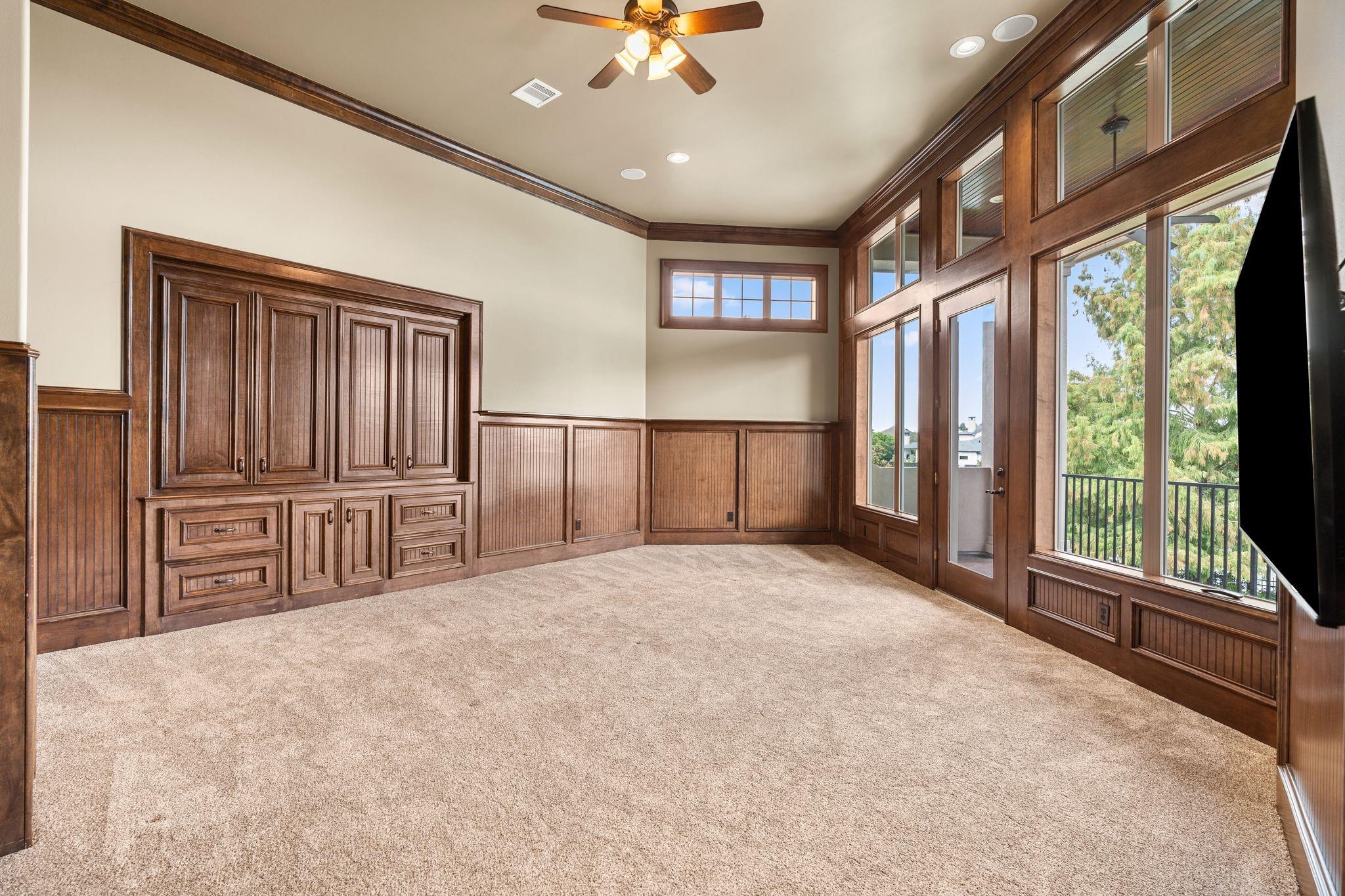 Carpeted room with dark wood built-ins and tall windows overlooking a balcony.