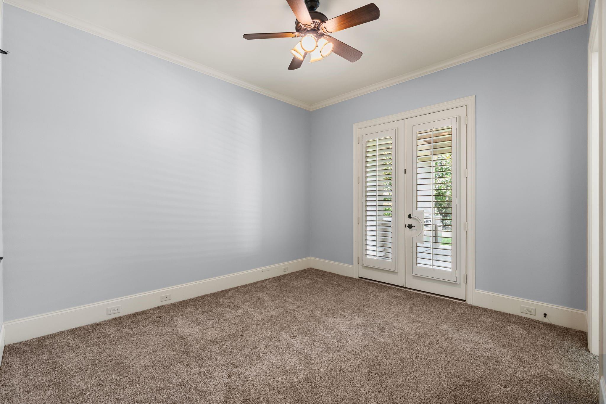 Empty carpeted room with shuttered double doors and a ceiling fan with lights.