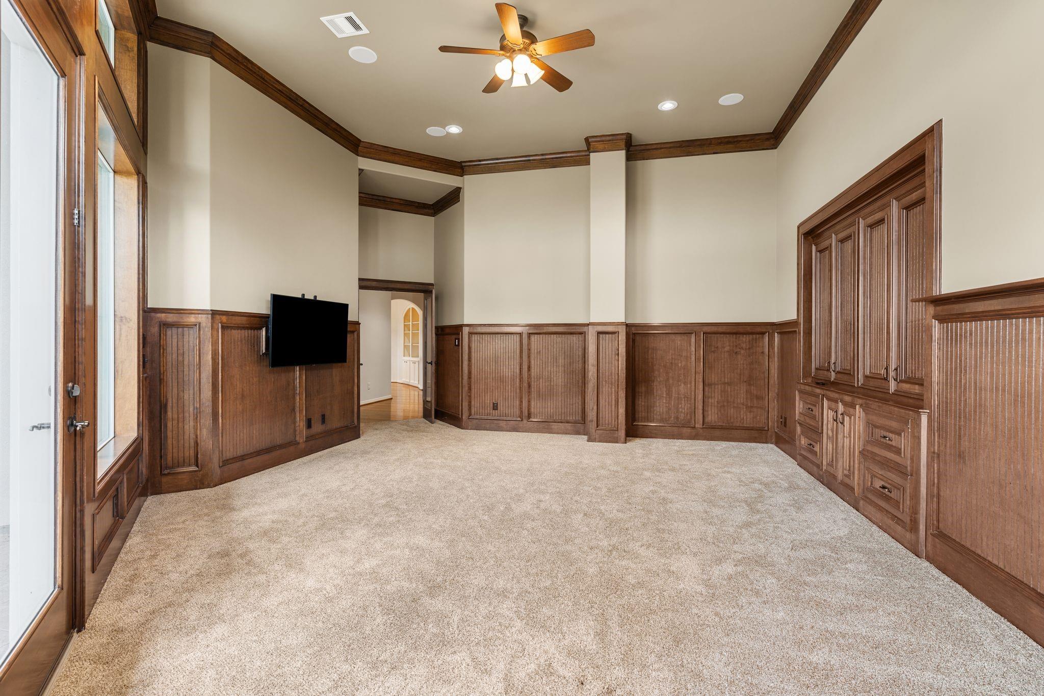 Empty media room with dark wood built-ins, a wall-mounted television, and tall windows.