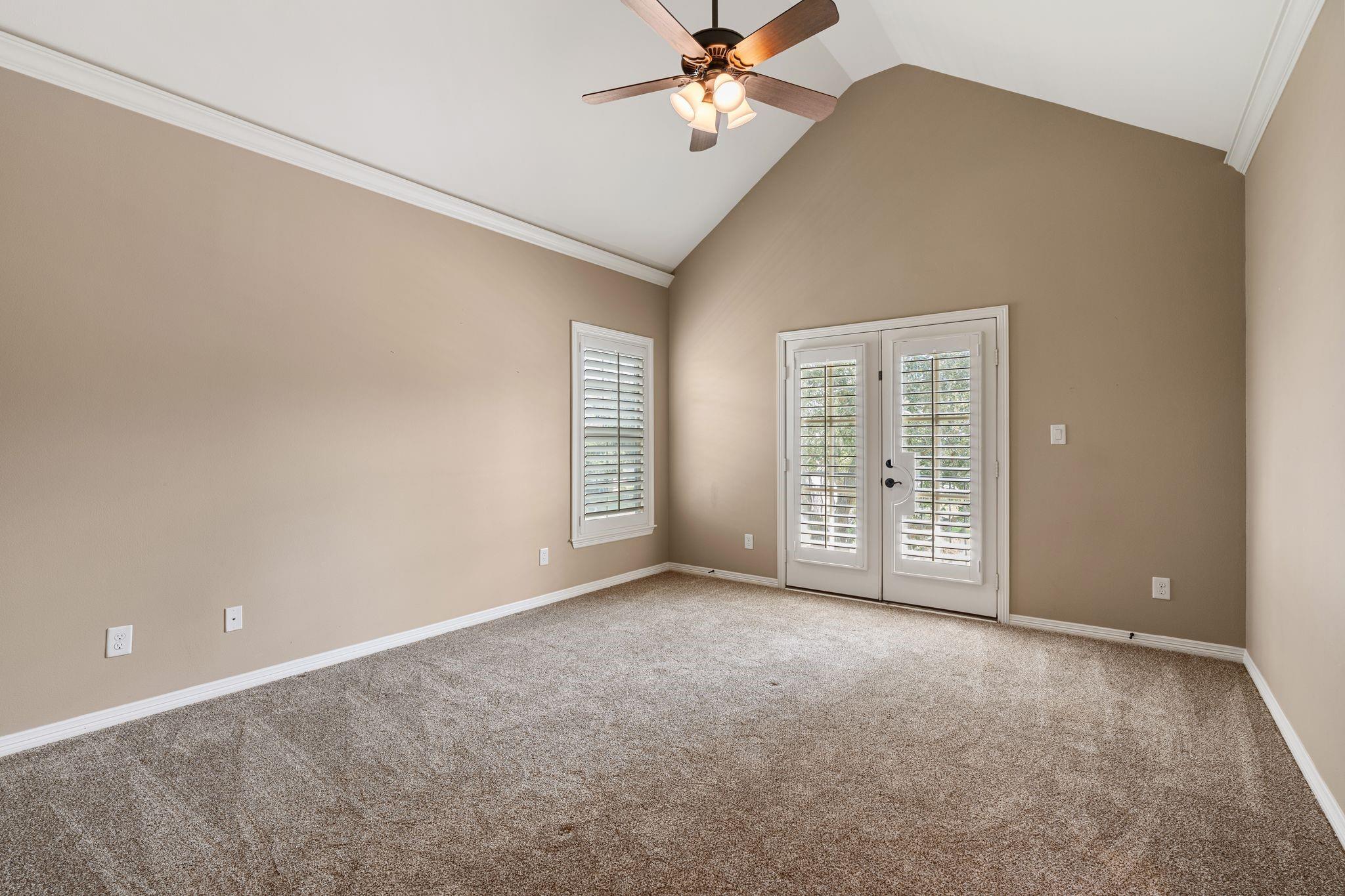 Empty carpeted room with a vaulted ceiling, ceiling fan, and shuttered double doors.