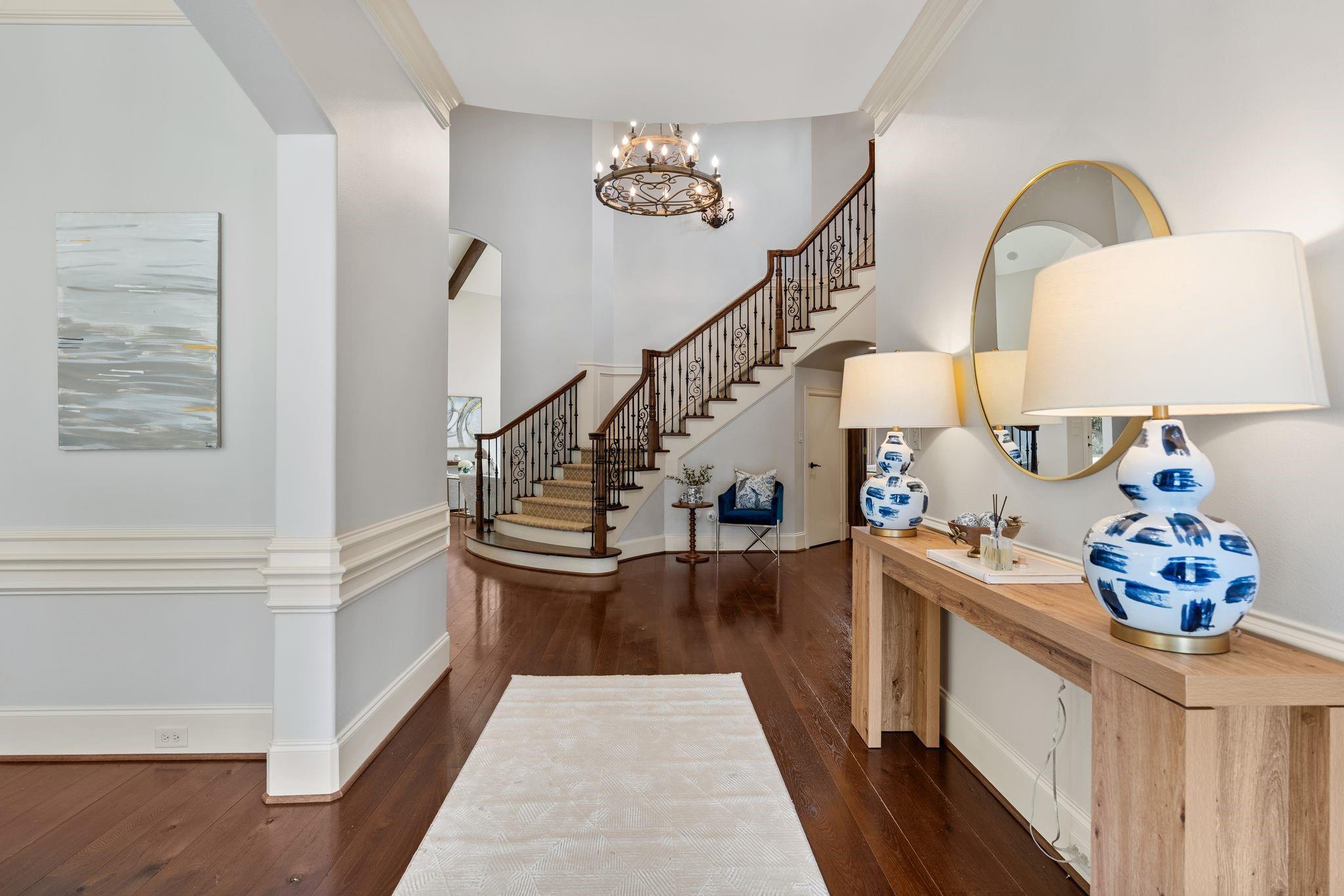 Entry foyer with a sweeping staircase, dark hardwood floors, and a console table with blue-and-white lamps.