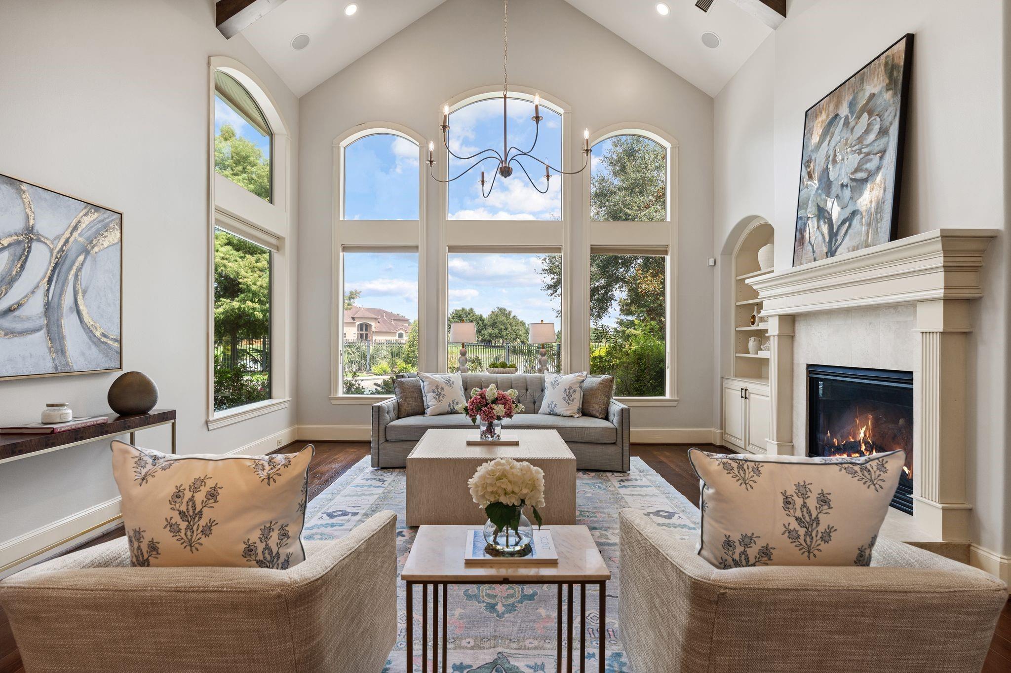 Staged living room with vaulted ceilings, tall arched windows, and a large fireplace.