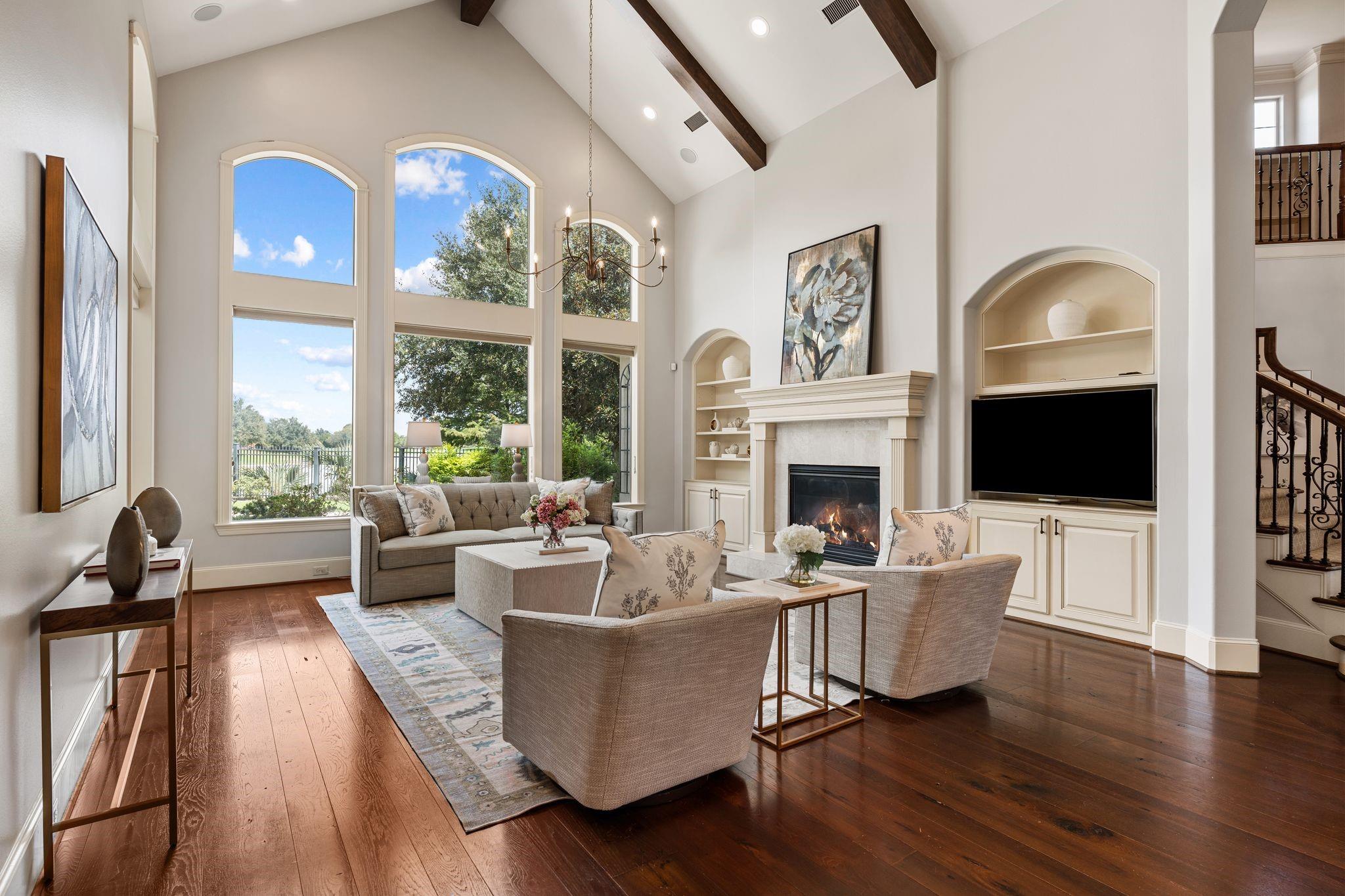 Living room with vaulted beamed ceiling, tall arched windows, fireplace, and built-in media cabinetry.