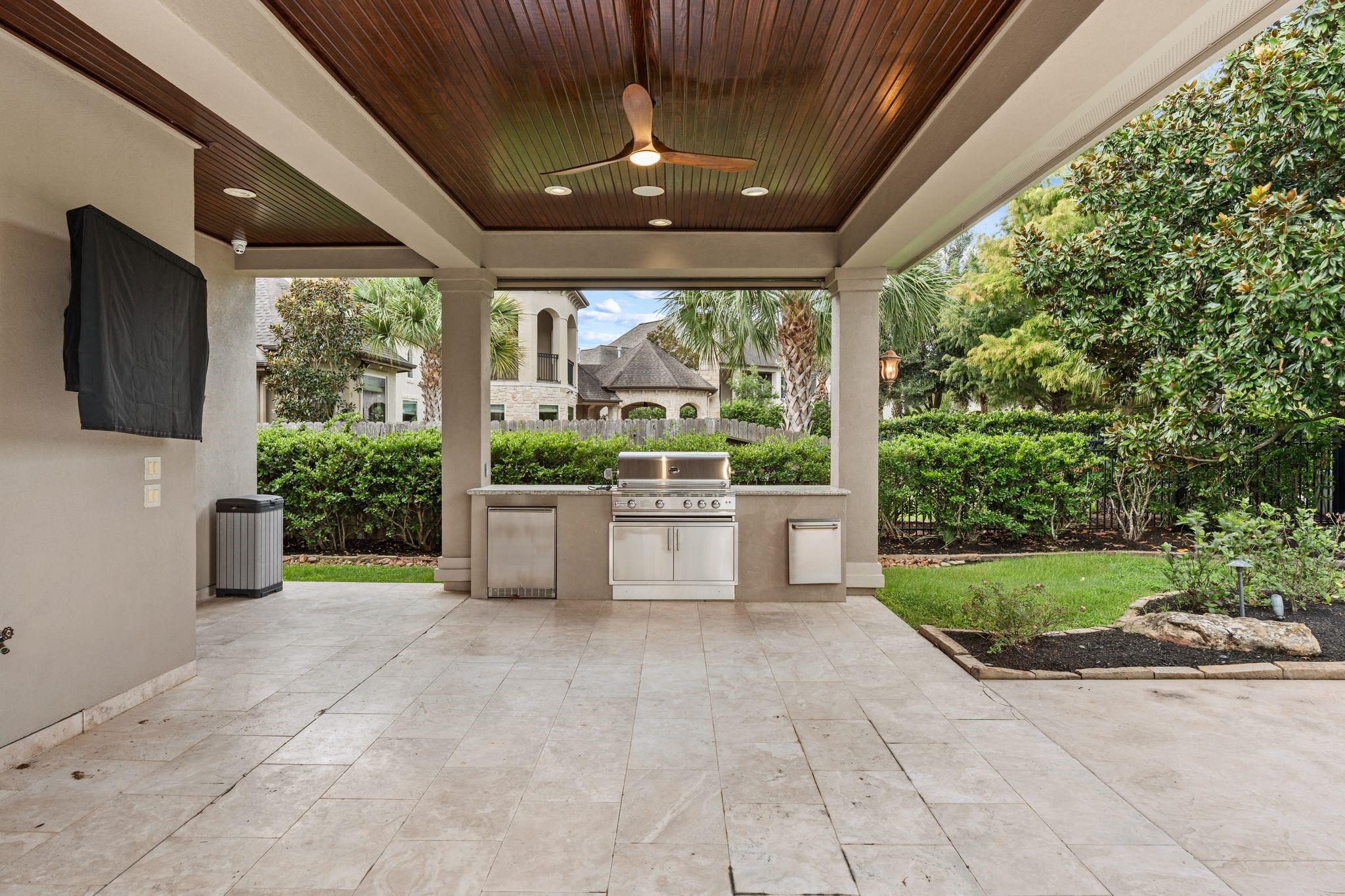 Covered patio with a wood-paneled ceiling, ceiling fan, and built-in stainless steel outdoor kitchen.