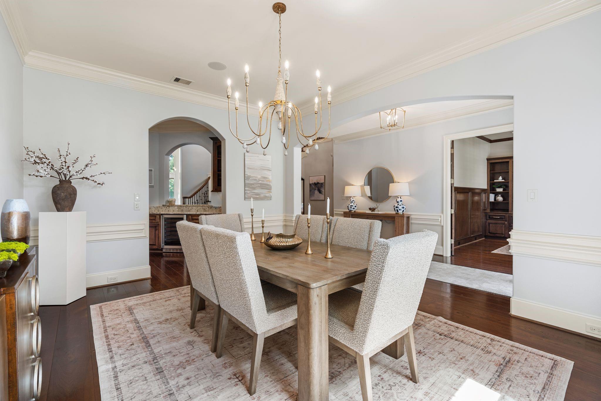 Dining room with a wood table, upholstered chairs, brass chandelier, and arched openings.
