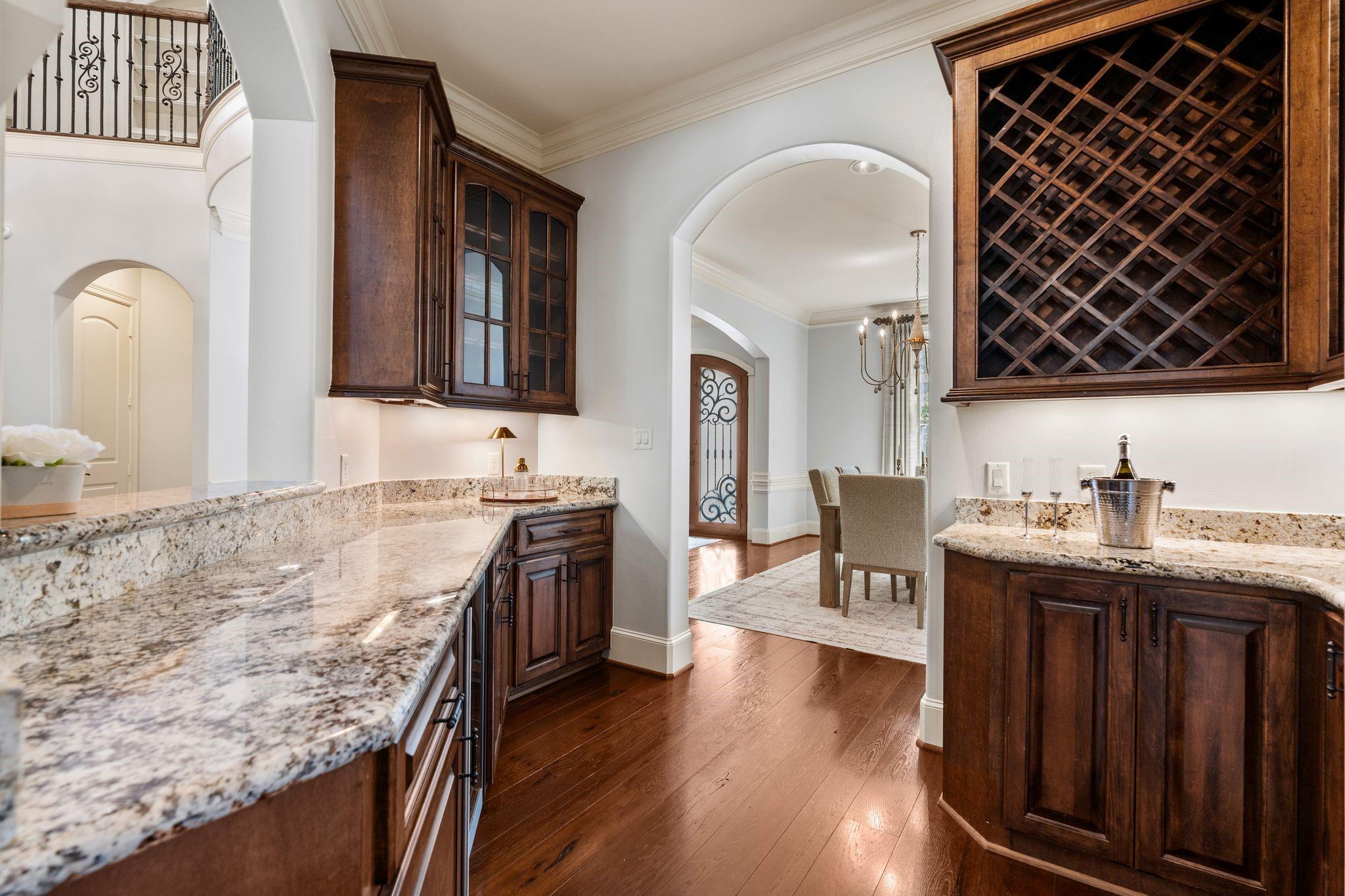 Kitchen with granite counters, dark wood cabinets, and a built-in wine rack beside an arched dining-room entrance.