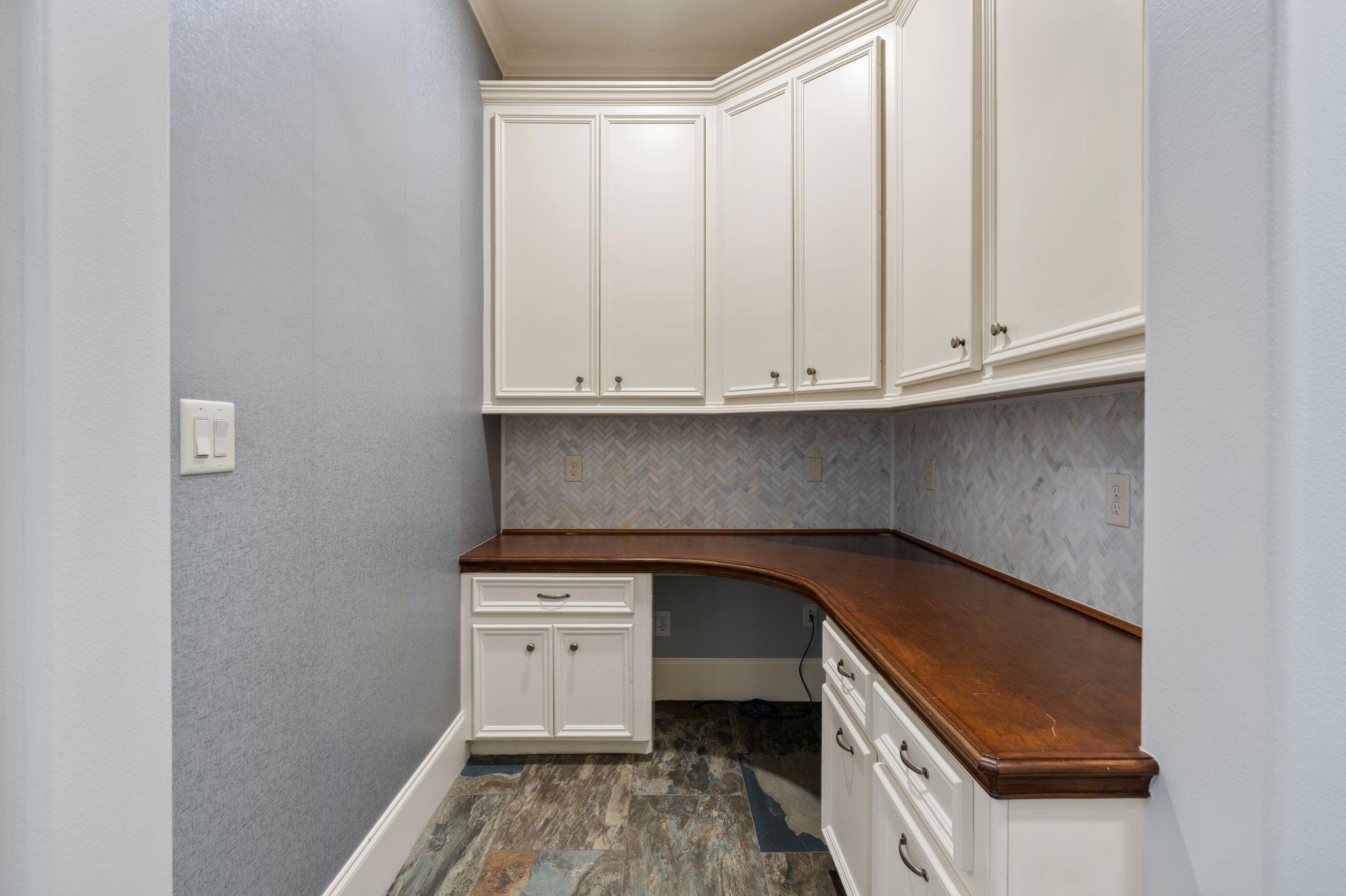 Built-in desk with white cabinets, curved dark wood counter, and herringbone tile backsplash.