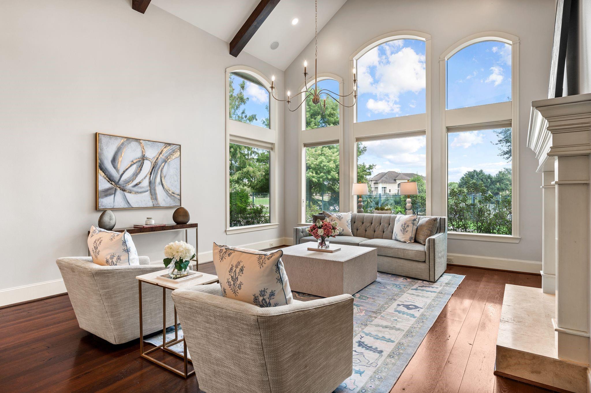 Staged living room with vaulted ceiling, tall arched windows, and seating around a large coffee table.