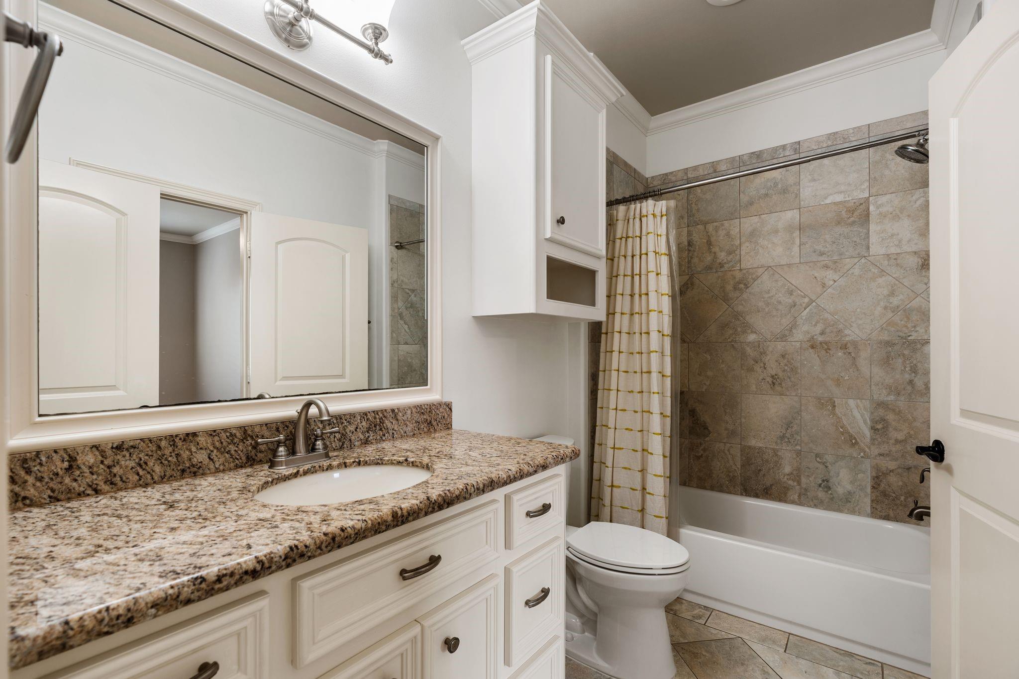 Bathroom with granite vanity, white cabinetry, and a stone-tiled tub and shower.