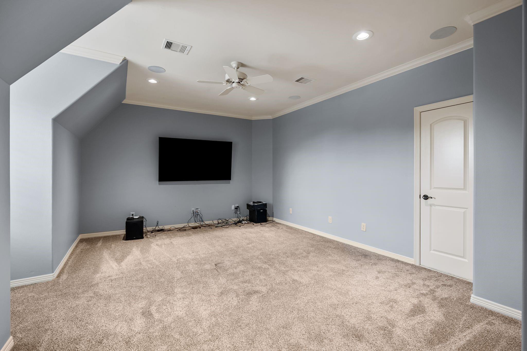 Unfurnished media room with a wall-mounted television, speakers, beige carpet, and ceiling fan.