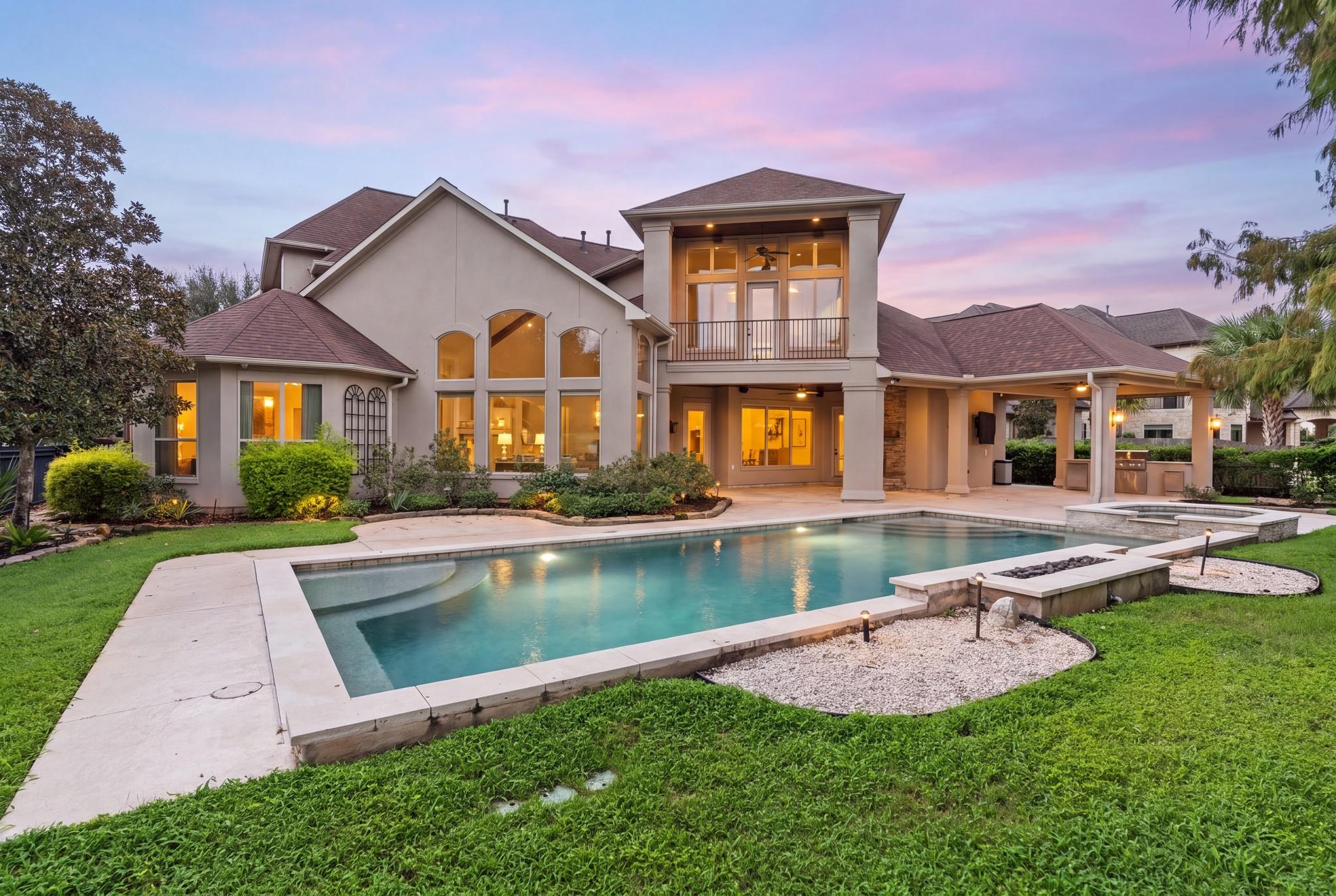 Two-story home overlooking a swimming pool, with a covered patio and landscaped lawn at dusk.