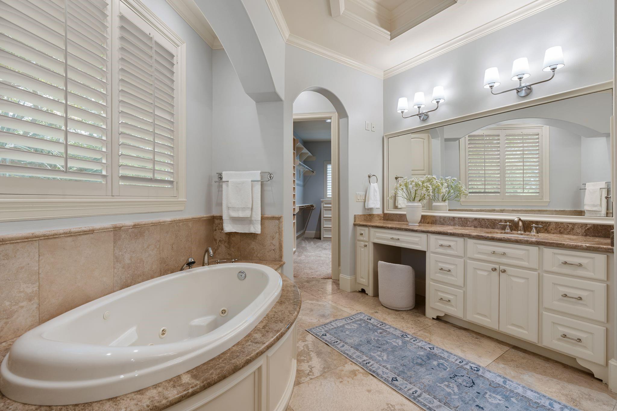 Primary bathroom with a large soaking tub, long double vanity, and arched walk-in closet doorway.