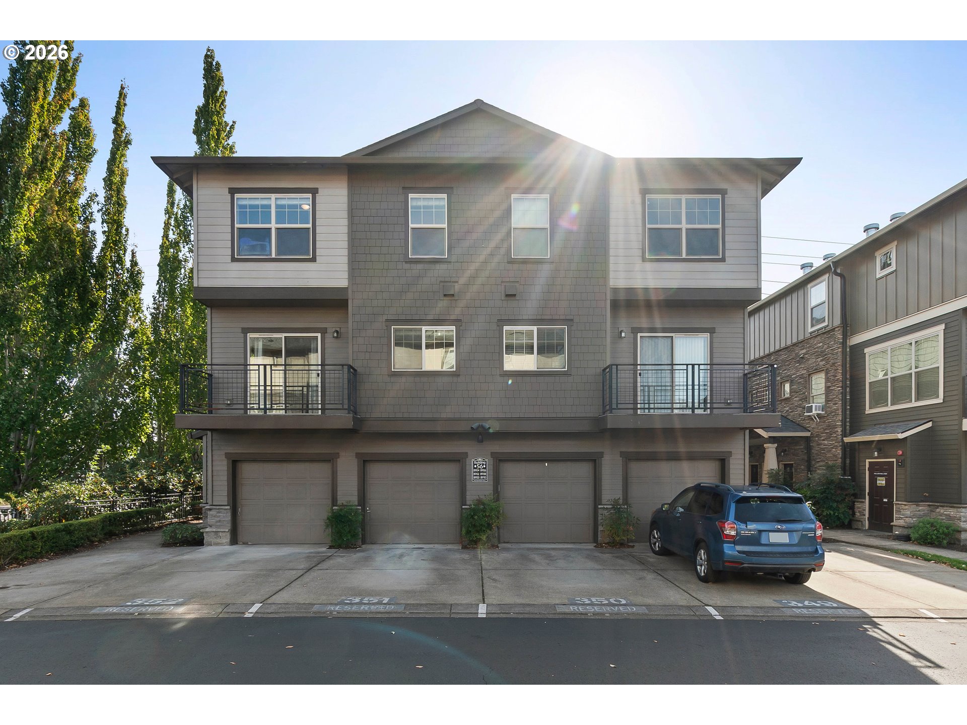 Gray multi-story residential building with balconies, garage doors, and a blue SUV parked out front.