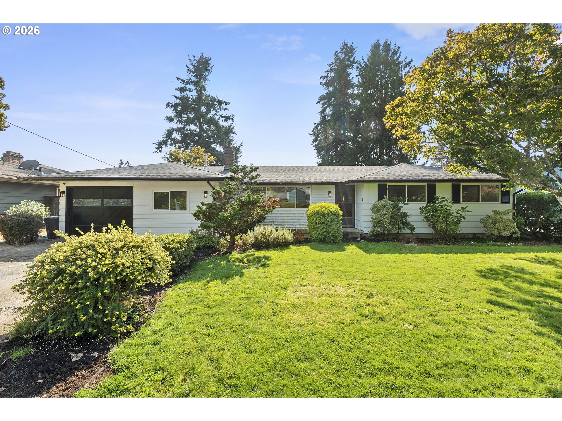Single-story home with a dark garage door, landscaped shrubs, and a broad green front lawn.