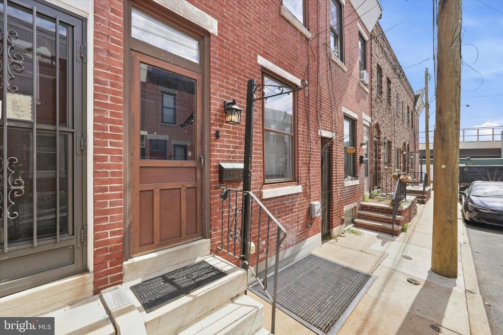 Red-brick Philadelphia rowhouse with a brown front door, stone stoop, and black metal railing.