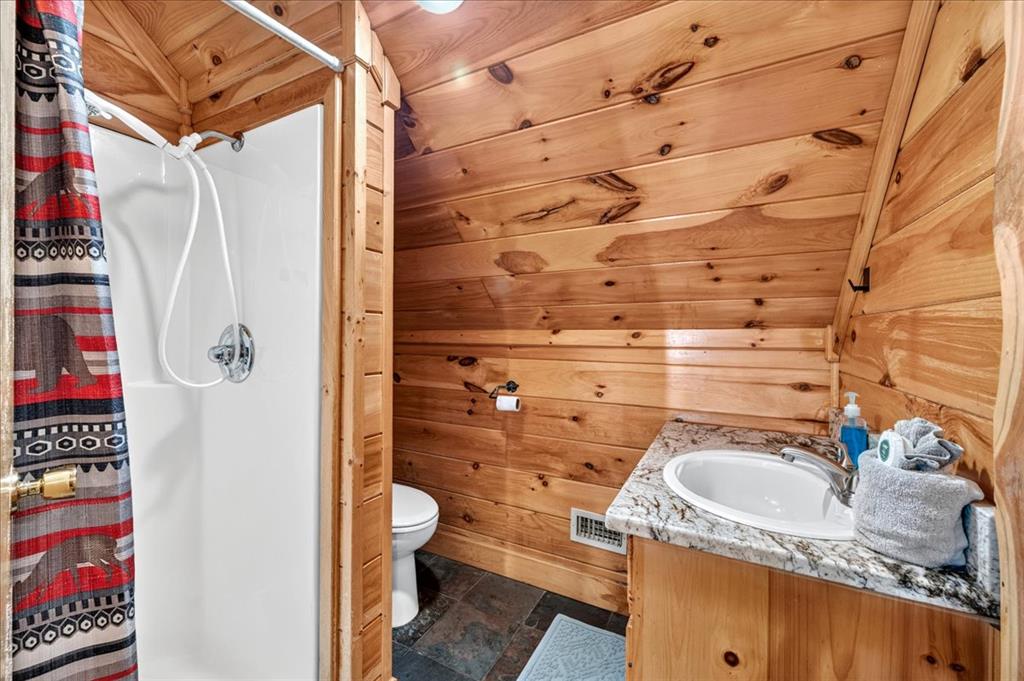 Cabin bathroom with knotty pine walls, a white shower, and a marble-look vanity.