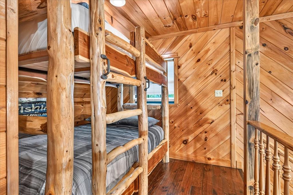 Rustic cabin bedroom with log bunk beds, knotty pine walls, and a wooden stair railing.