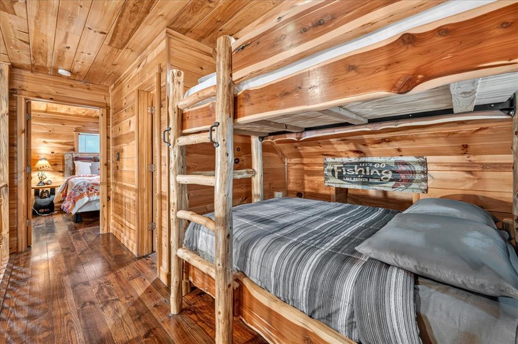 Wood-paneled cabin bedroom with a wooden bunk bed, ladder, and gray striped bedding.