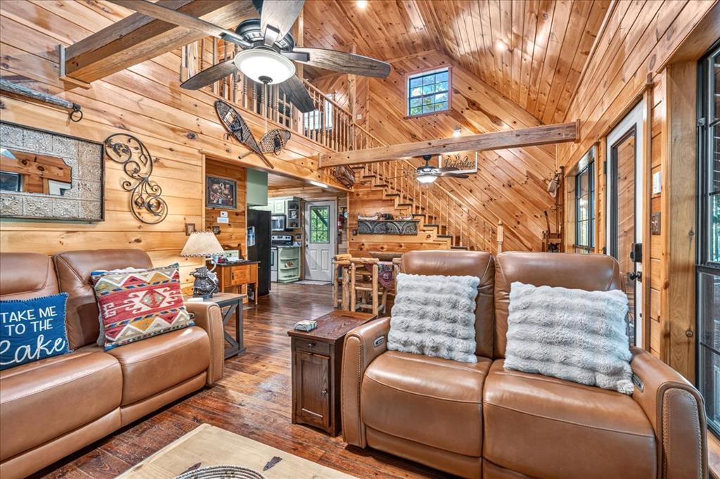 Cabin living room with leather sofas, vaulted wood ceiling, loft staircase, and open kitchen.