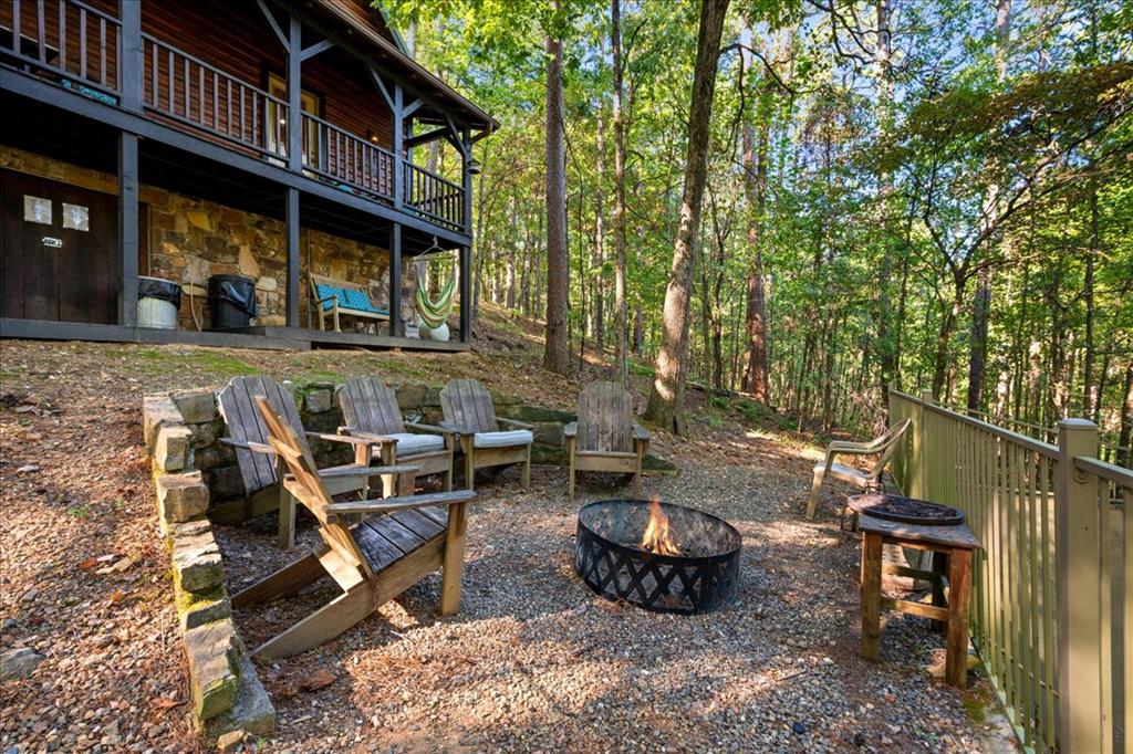 Cabin patio with Adirondack chairs around a fire pit, surrounded by trees.
