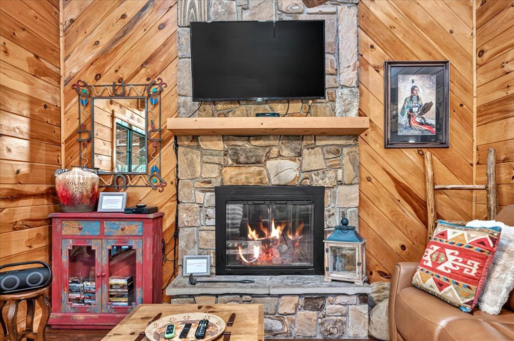 Living room with stone fireplace, mounted TV, and warm wood-paneled walls.