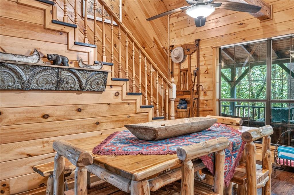 Rustic log dining area with a wooden table, staircase, and large windows overlooking trees.