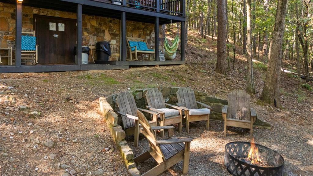 Wooded cabin porch overlooks Adirondack chairs around a lit fire pit.