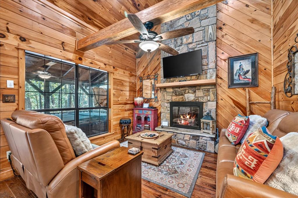 Cabin living room with a stone fireplace, wood-paneled walls, leather seating, and large windows.