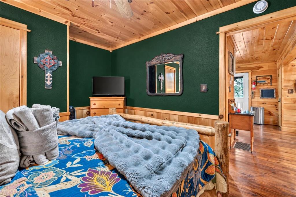 Bedroom with a log-frame bed, patterned bedding, dark green walls, and a knotty-pine ceiling.