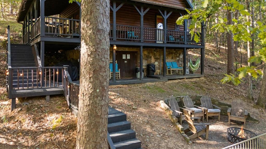 Two-story cabin with a covered deck and fire pit seating in a wooded setting.