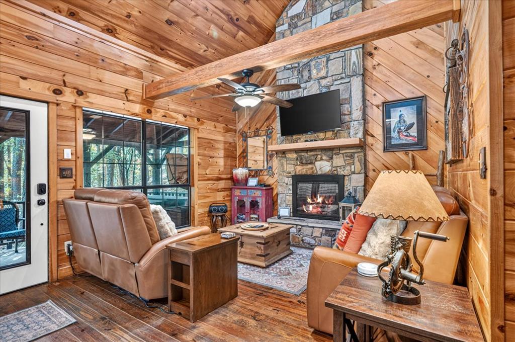 Living room with knotty-pine walls, leather seating, and a stone fireplace beneath a television.
