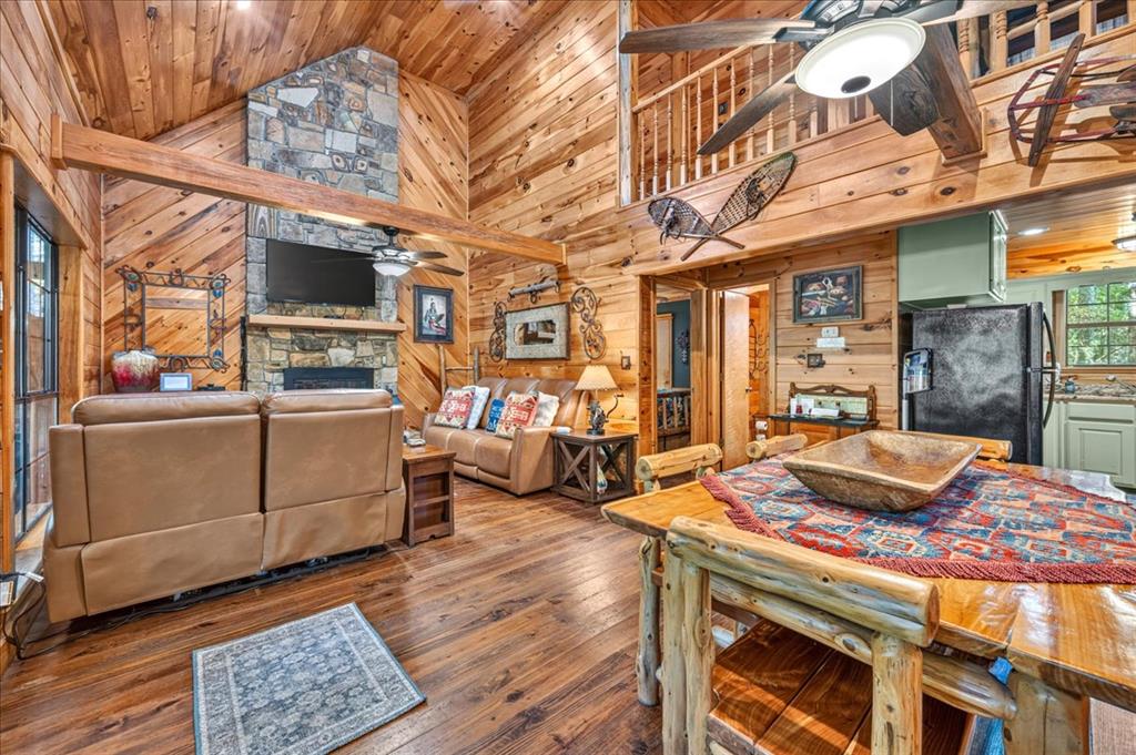 Cabin living room with vaulted wood ceiling, stone fireplace, leather sofas, and rustic dining table.