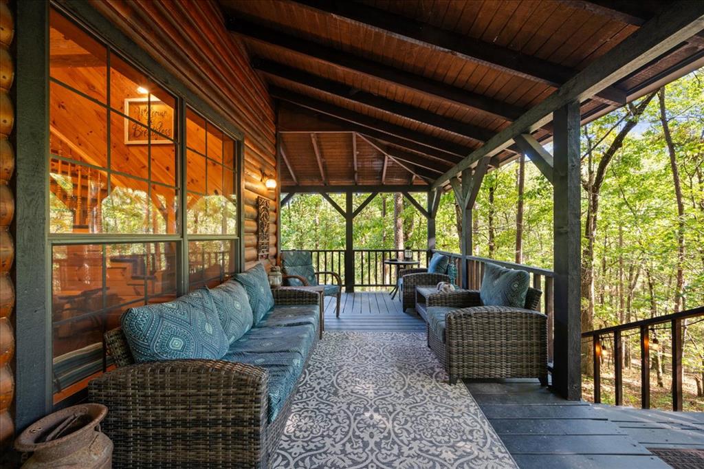 Covered cabin porch with wicker seating, blue cushions, a patterned rug, and woodland views.