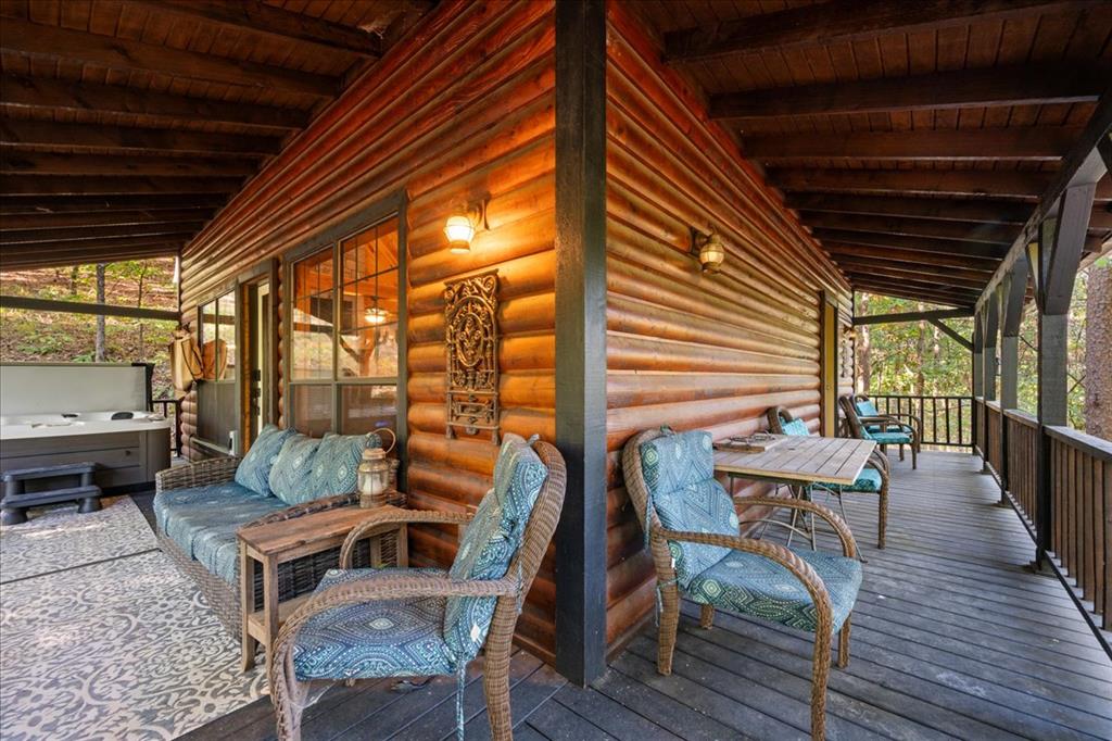 Covered log-cabin porch with cushioned wicker seating, a dining table, and a hot tub.