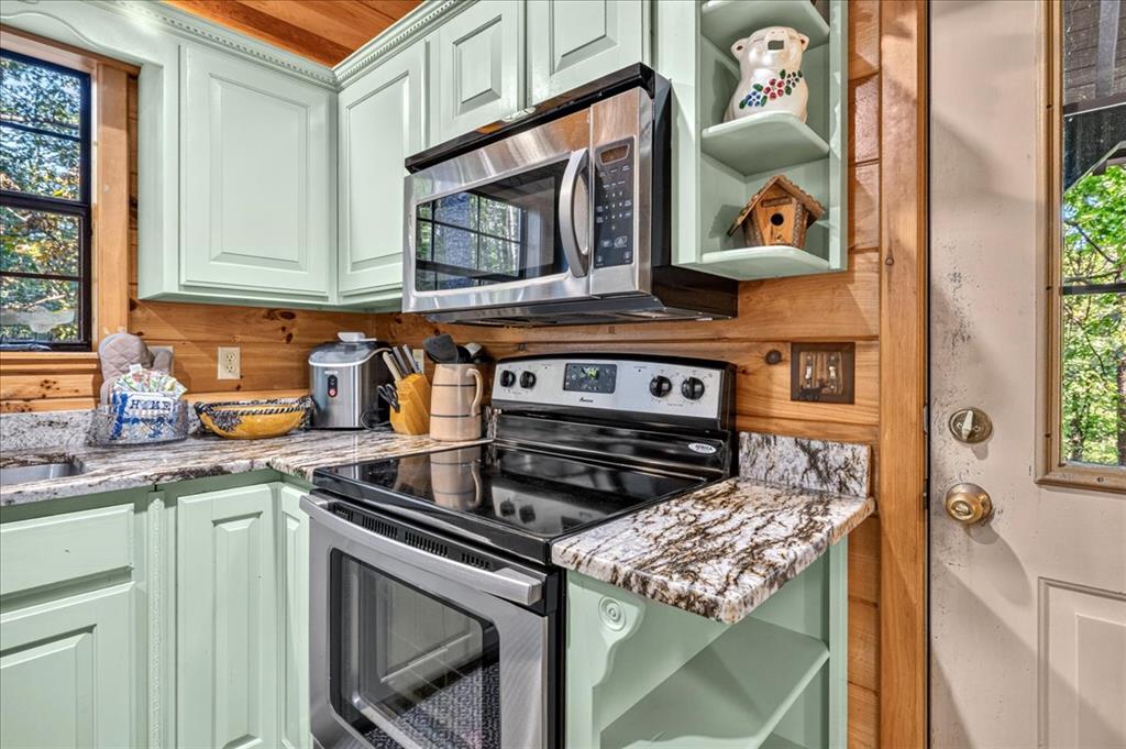 Kitchen with mint-green cabinets, granite countertops, stainless-steel appliances, and warm wood-paneled walls.
